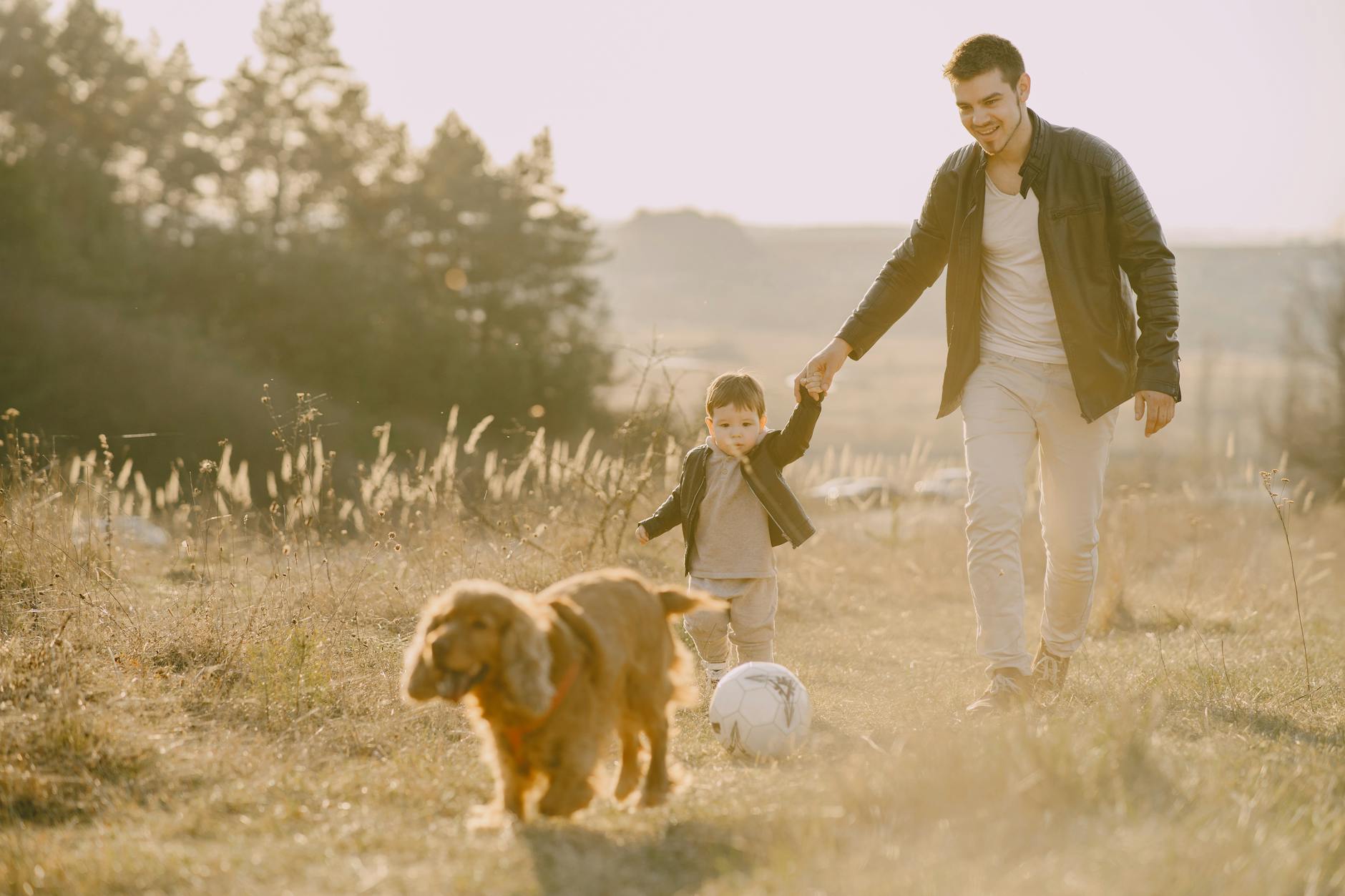 A dad holding his child's hand while walking the dog